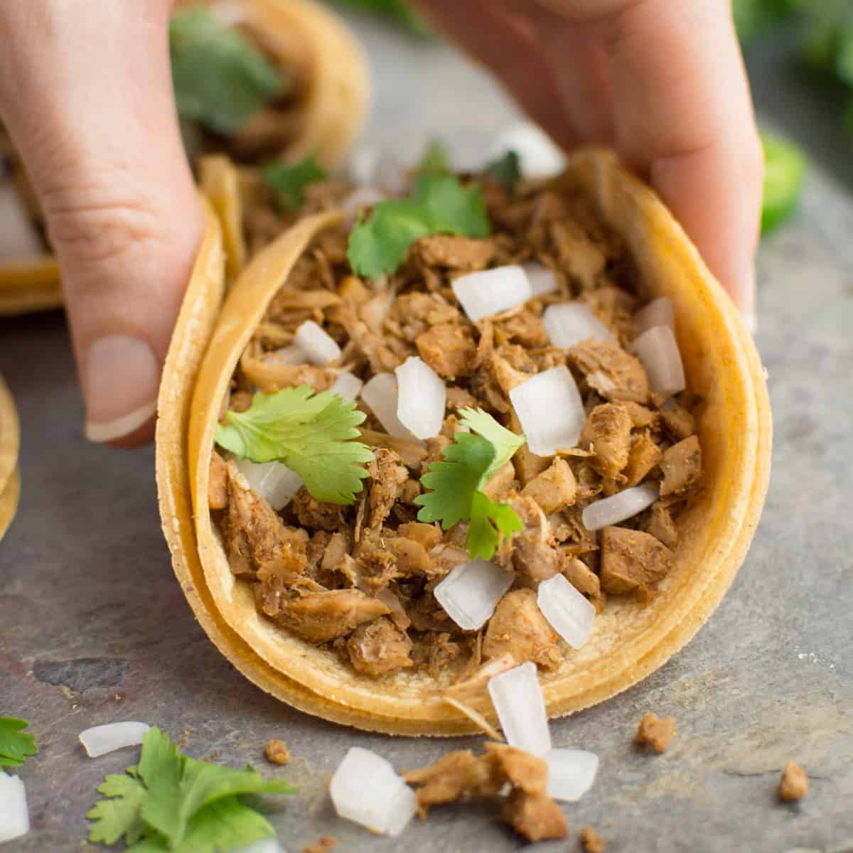 A hand folding up a vegan taco filled with jackfruit meat, onion, and cilantro.