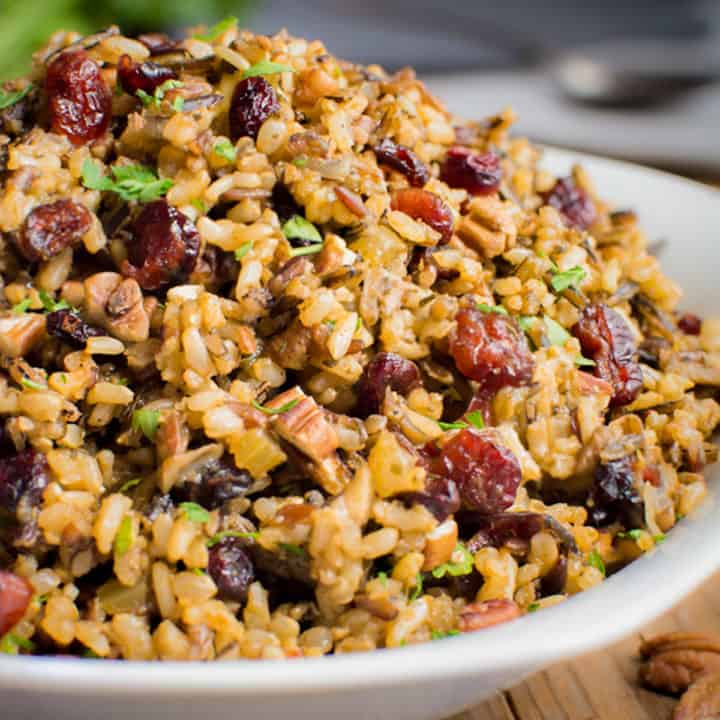 Wild rice stuffing with celery, cranberries and toasted pecans in white bowl.