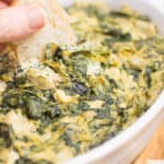 baguette being dipped in vegan spinach artichoke dip.