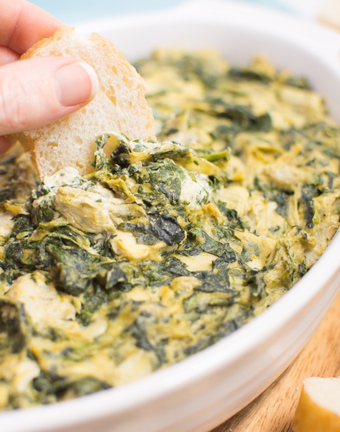 baguette being dipped in vegan spinach artichoke dip.