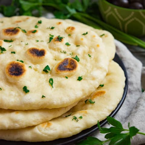 Soft vegan naan bread stacked on a plate.