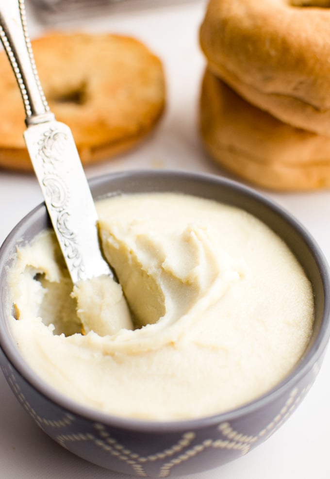 A small gray bowl filled with cashew cream cheese and a knife digging into it.