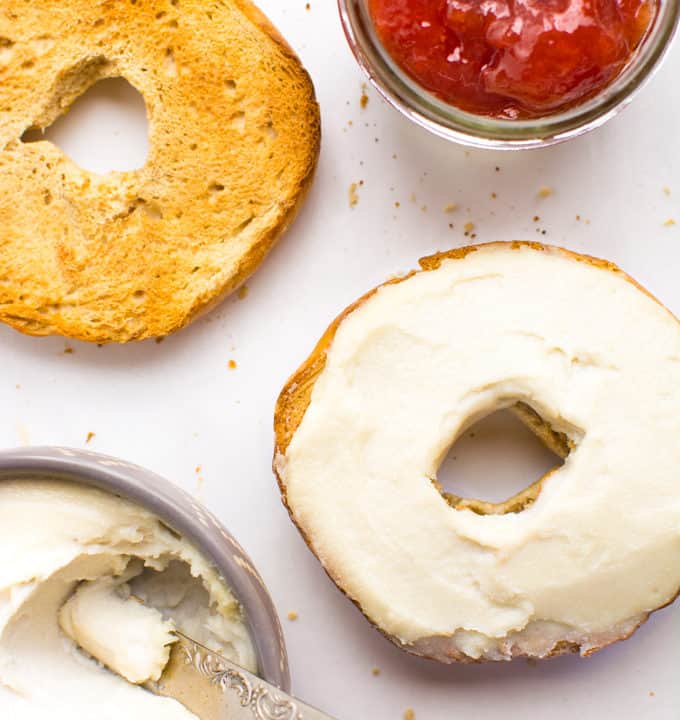 Cashew cream cheese spread on half a toasted bagel with a side of strawberry preserves.