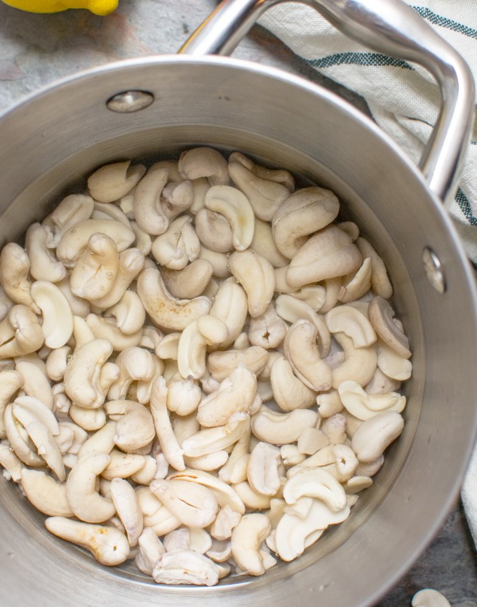 A stainless steel saucepan with cashews soaking in hot water for cream cheese.