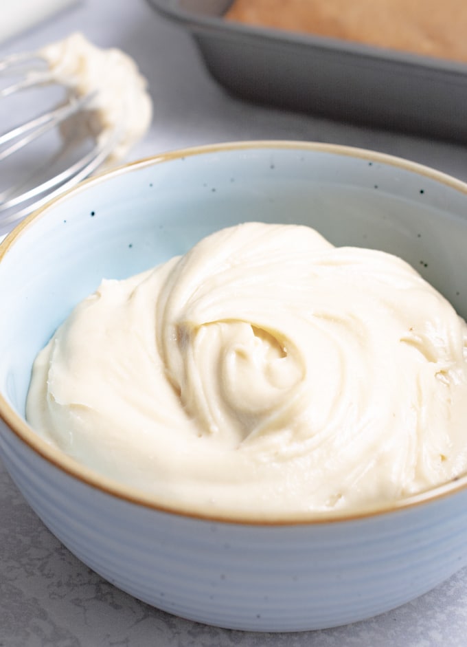 Fresh batch of cashew frosting in a blue bowl with an unfrosted cake near by.