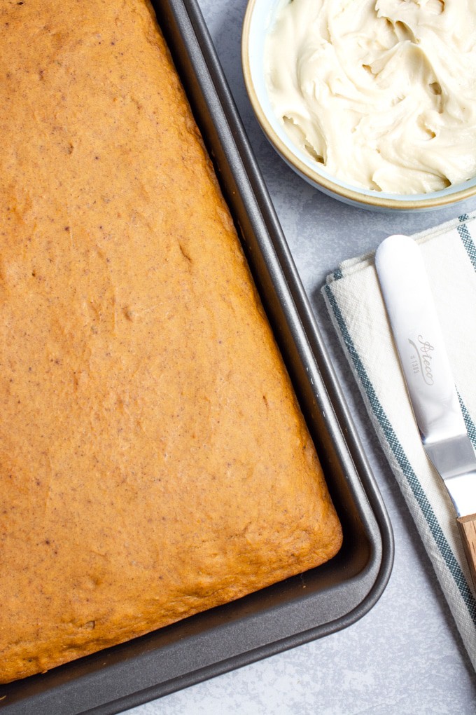 A sheet cake next to a bowl of frosting and an icing spatula.