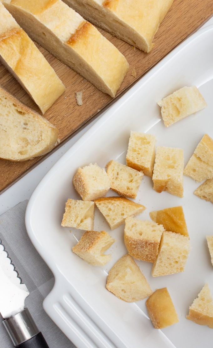 French loaf being cubed and added to a white baking dish.