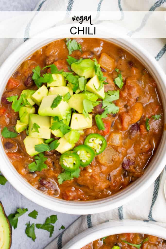 Vegan bean chili in a bowl topped with diced avocado, cilantro , and jalapeño peppers.