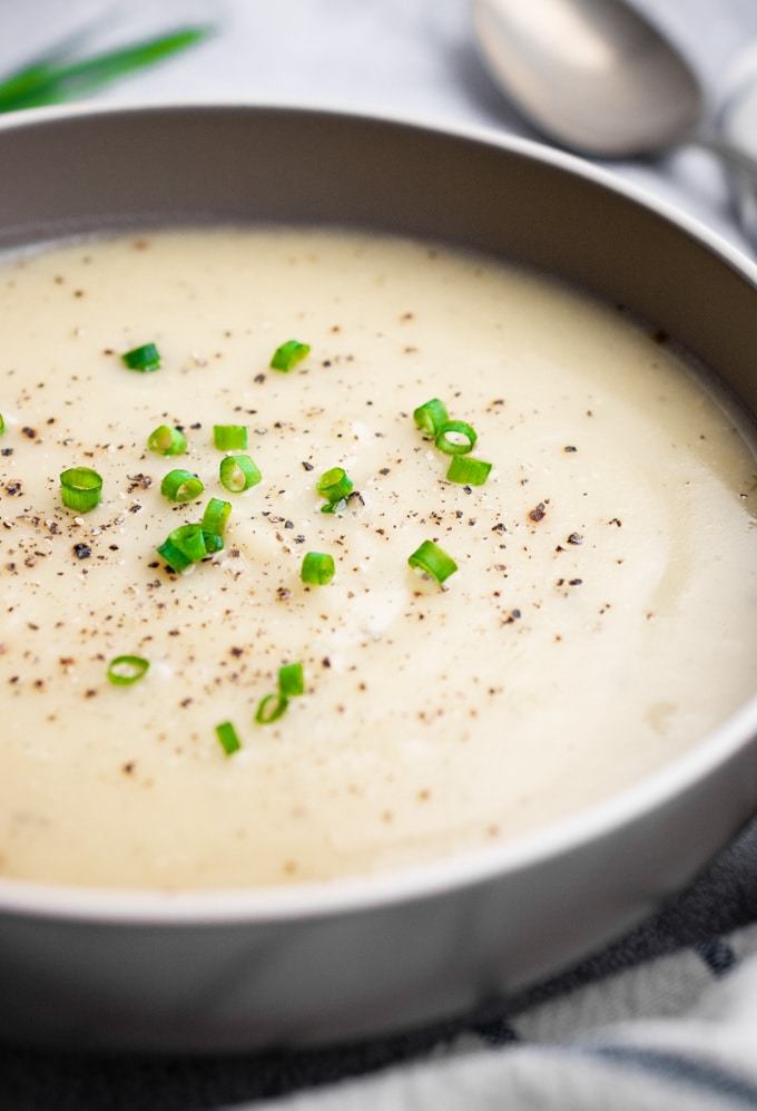 Instant Pot vegan potato soup in a gray bowl topped with green onions and fresh pepper.