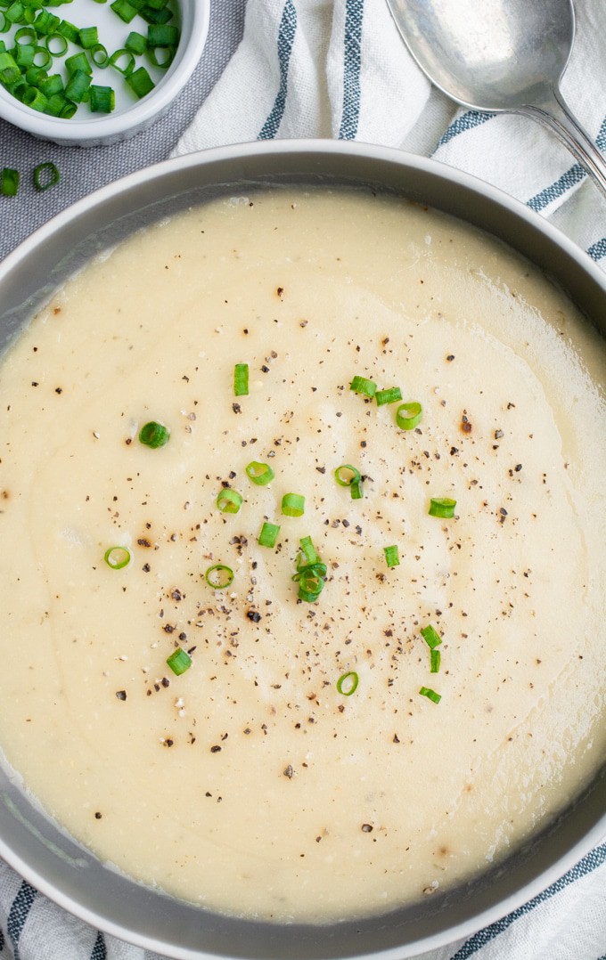 A bowl of potato soup topped with green onions and freshly ground black pepper.