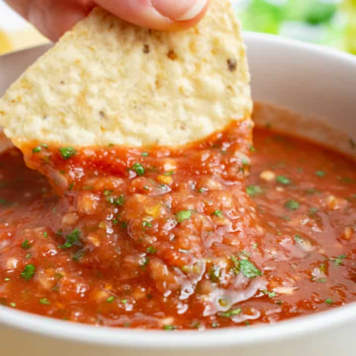 Tortilla chip scooping salsa from a bowl.