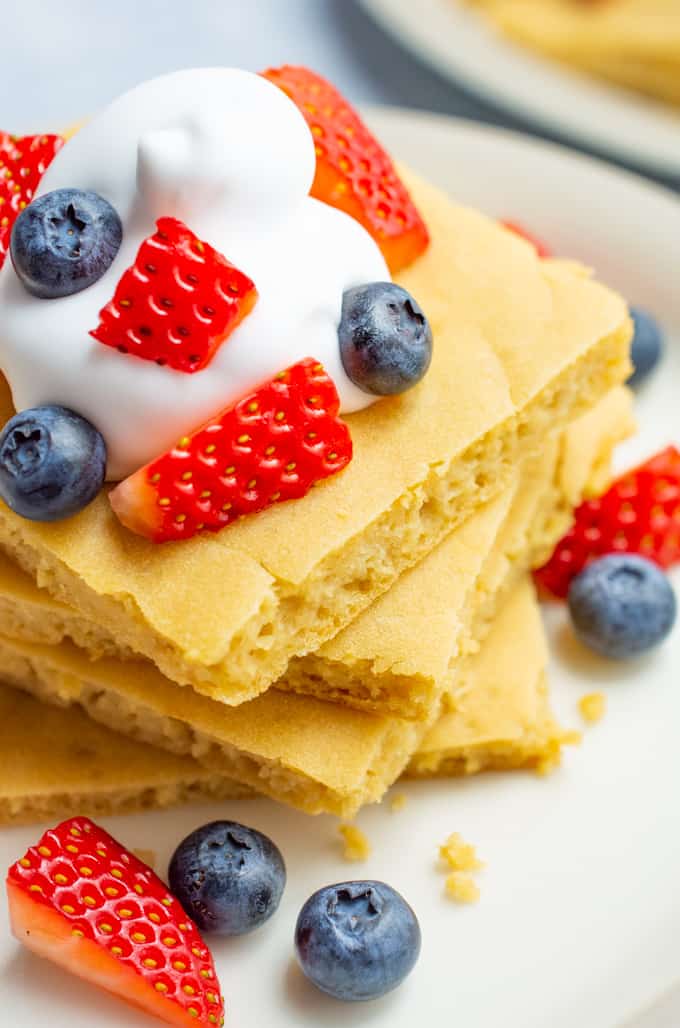 A stack of square pancakes with fruit and whip.