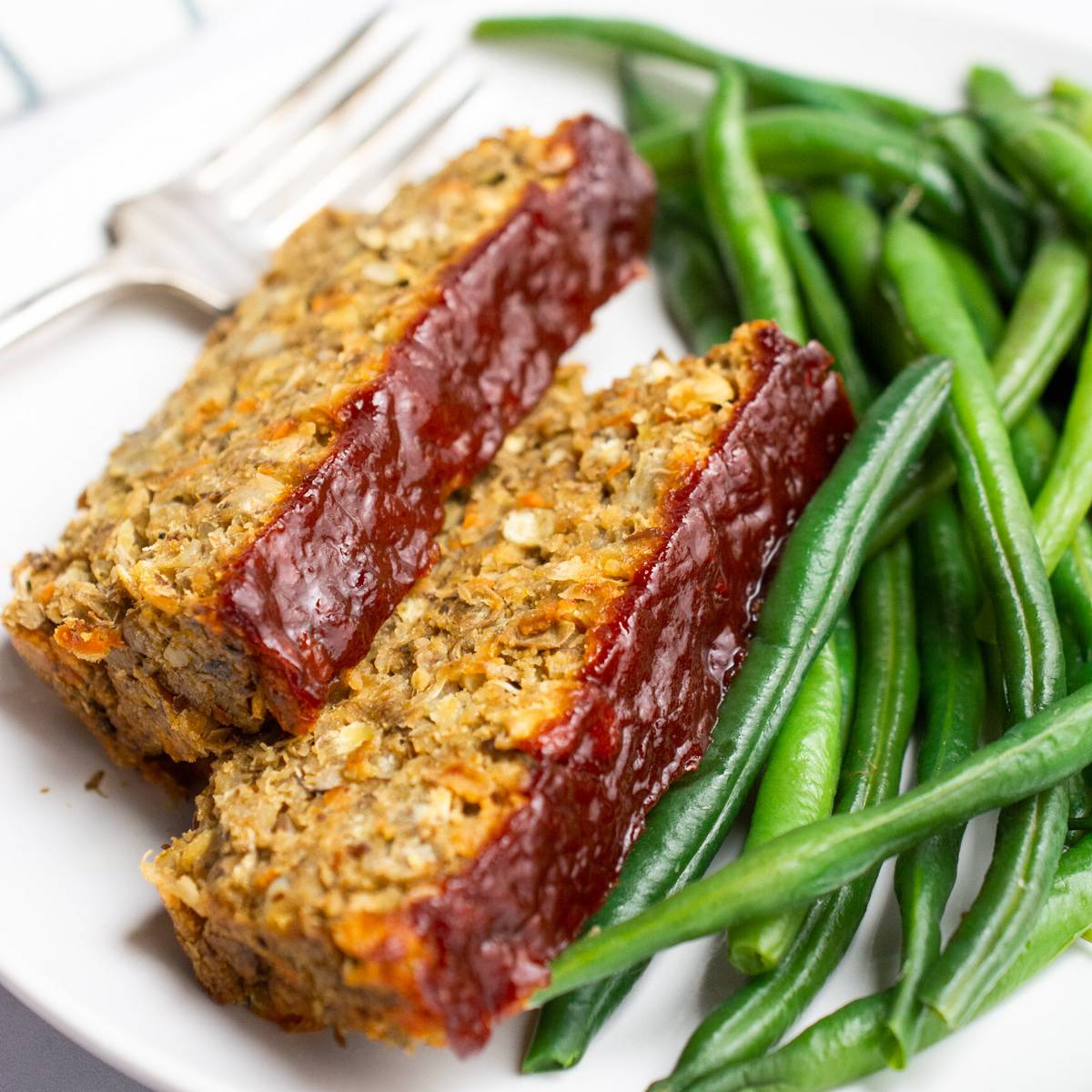 Vegan lentil loaf topped with ketchup and served with green beans.