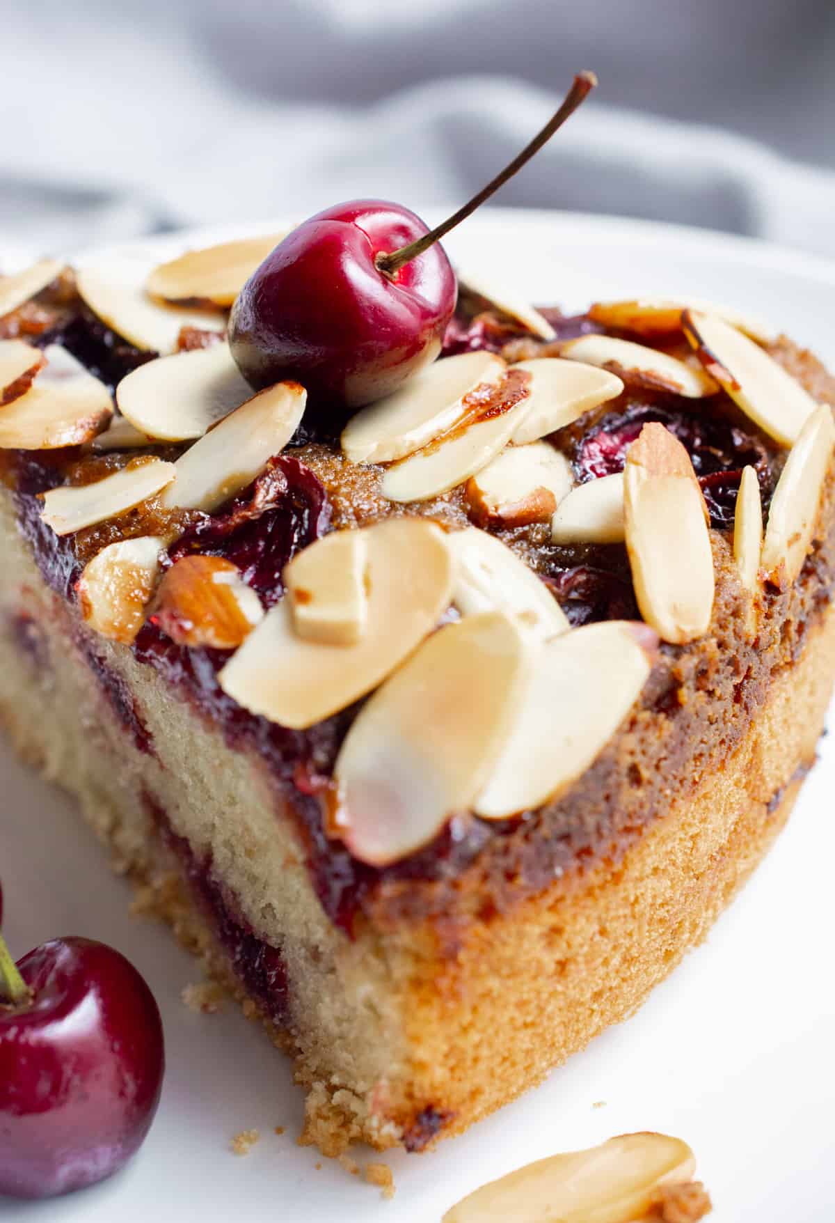 A slice of vegan coffee cake topped with fresh cherries and toasted almond slivers.