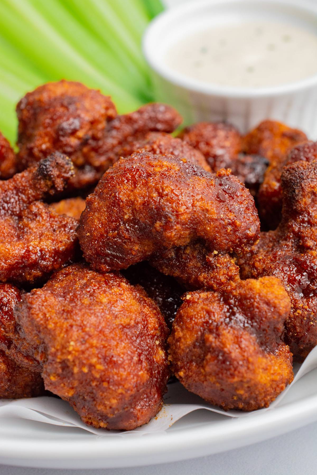 BBQ cauliflower wings on a plate with vegan ranch and celery sticks.