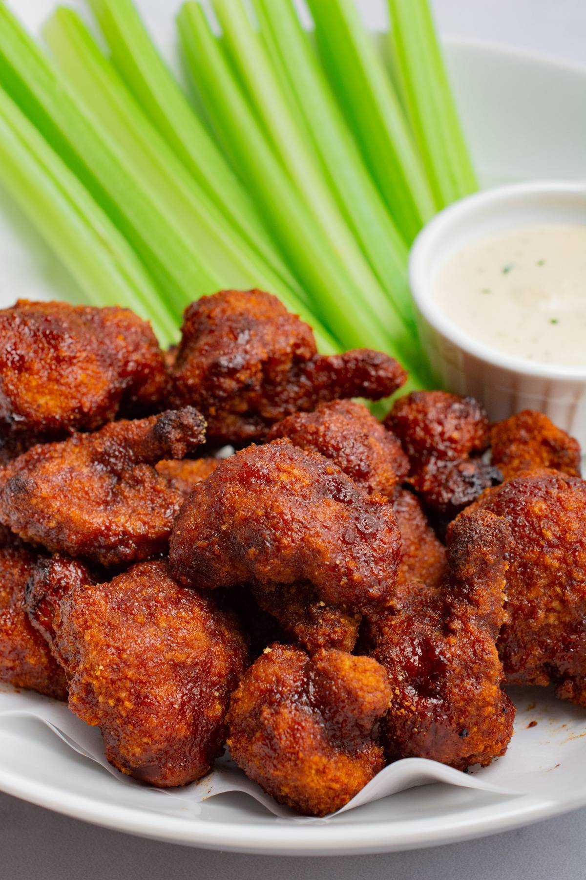 Vegan cauliflower wings on a plate with celery sticks and cheesy ranch.