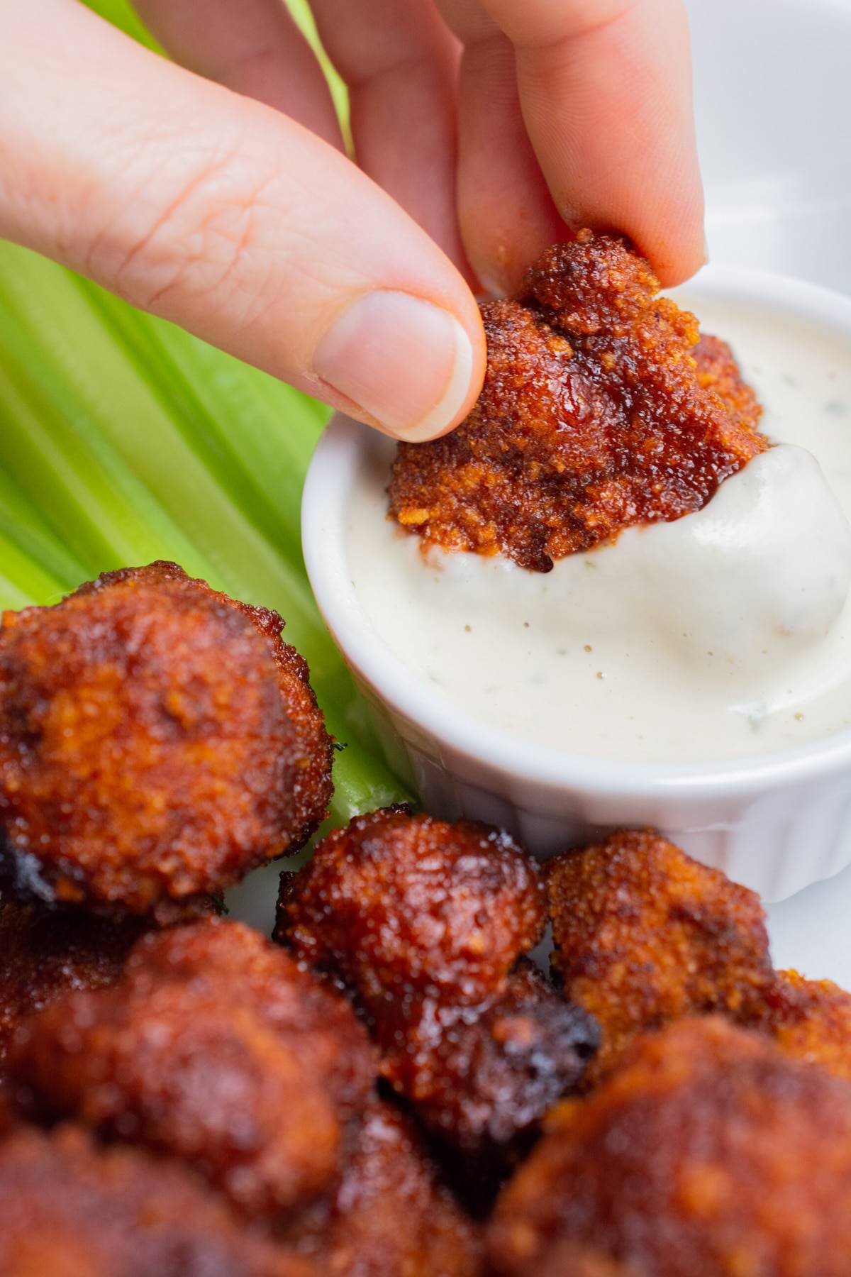 A hand dipping a BBQ Cauliflower wing in ranch.