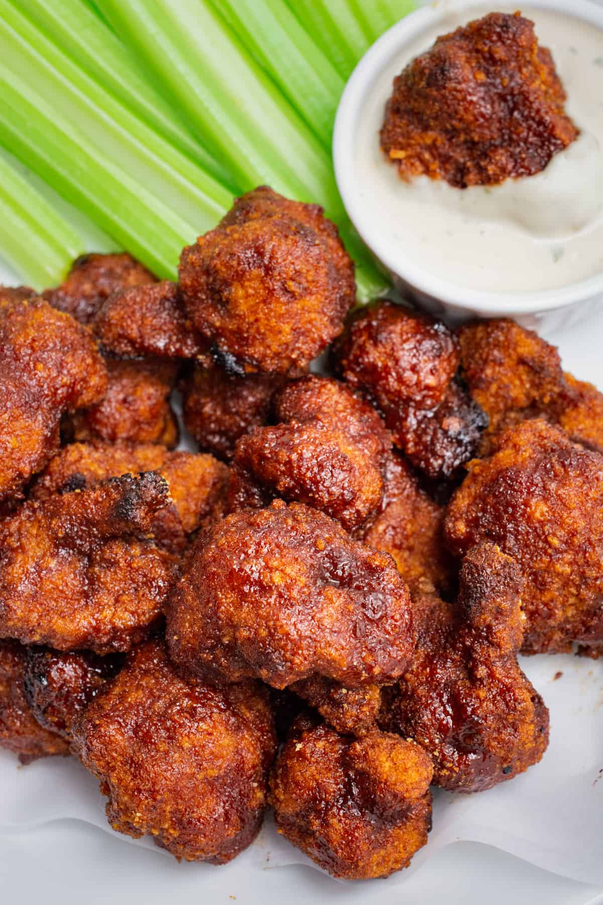 A plate of BBQ cauliflower wings, celery sticks, and a wing dipped in ranch.