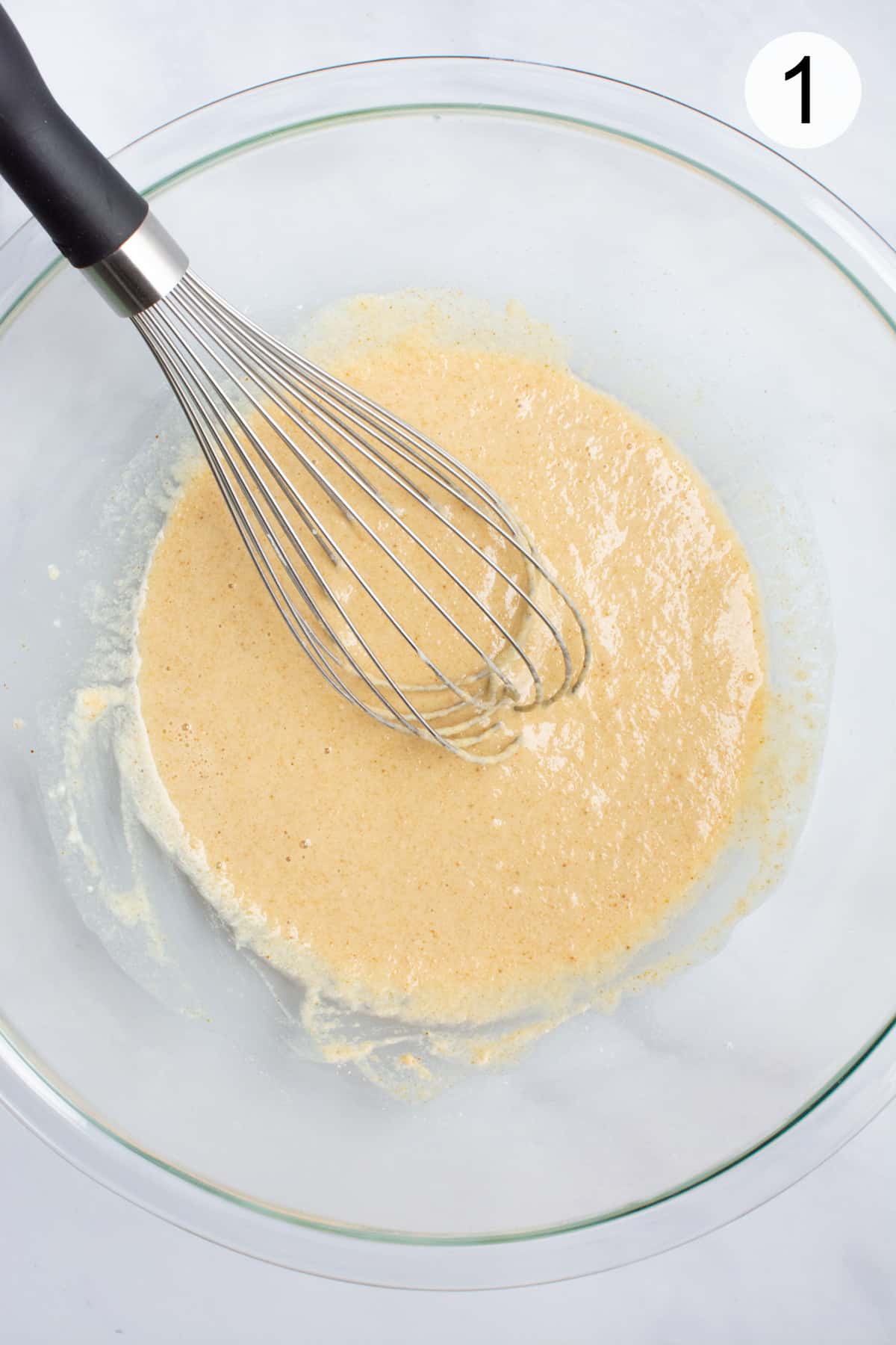 Batter mixed with a whisk in a glass bowl.