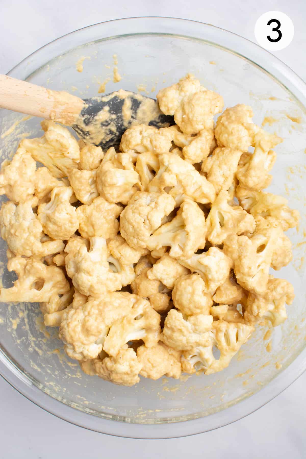 cauliflower in a glass bowl after tossing in batter.