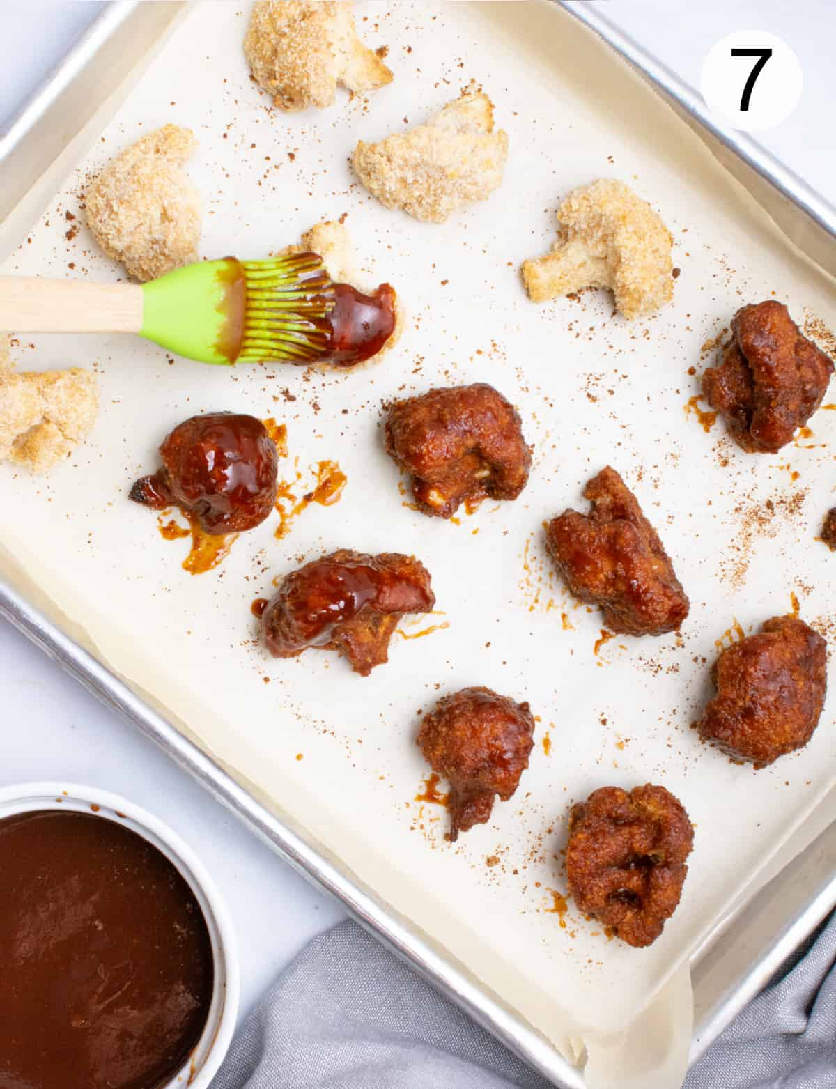 A pan of breaded cauliflower wings being brushed with BBQ sauce.