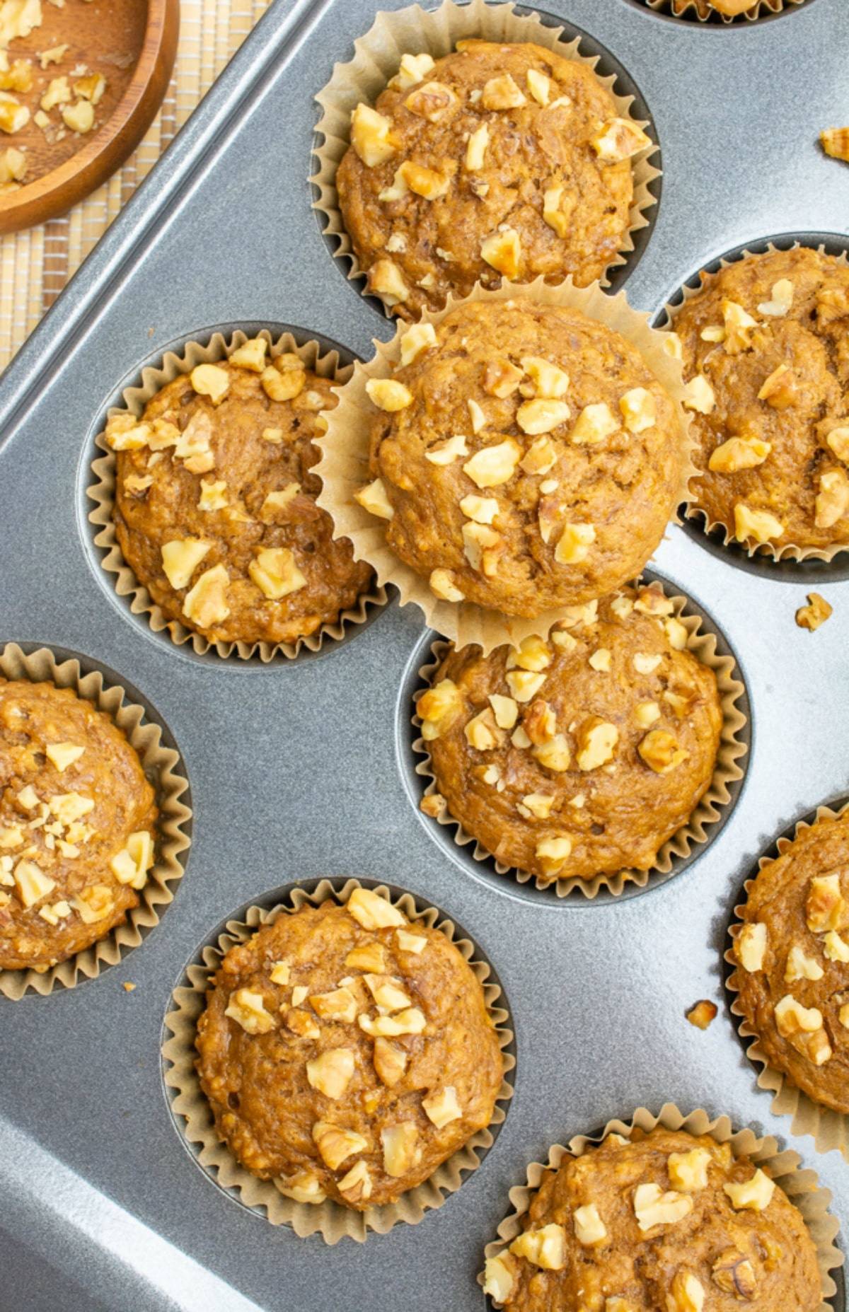 Vegan banana muffins topped with walnuts in a muffin pan.