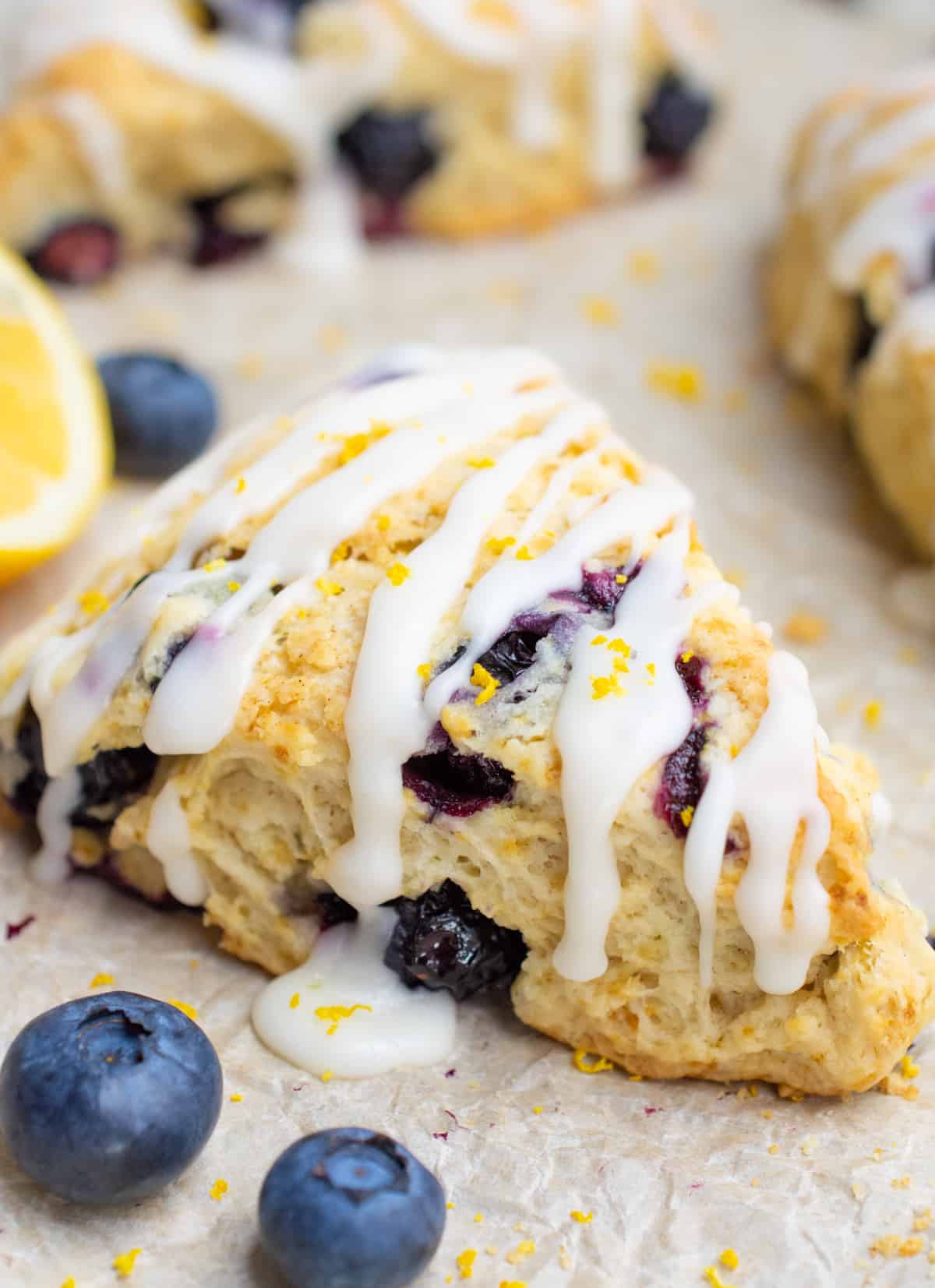 Vegan blueberry scone surrounded with lemon zest and blueberries.