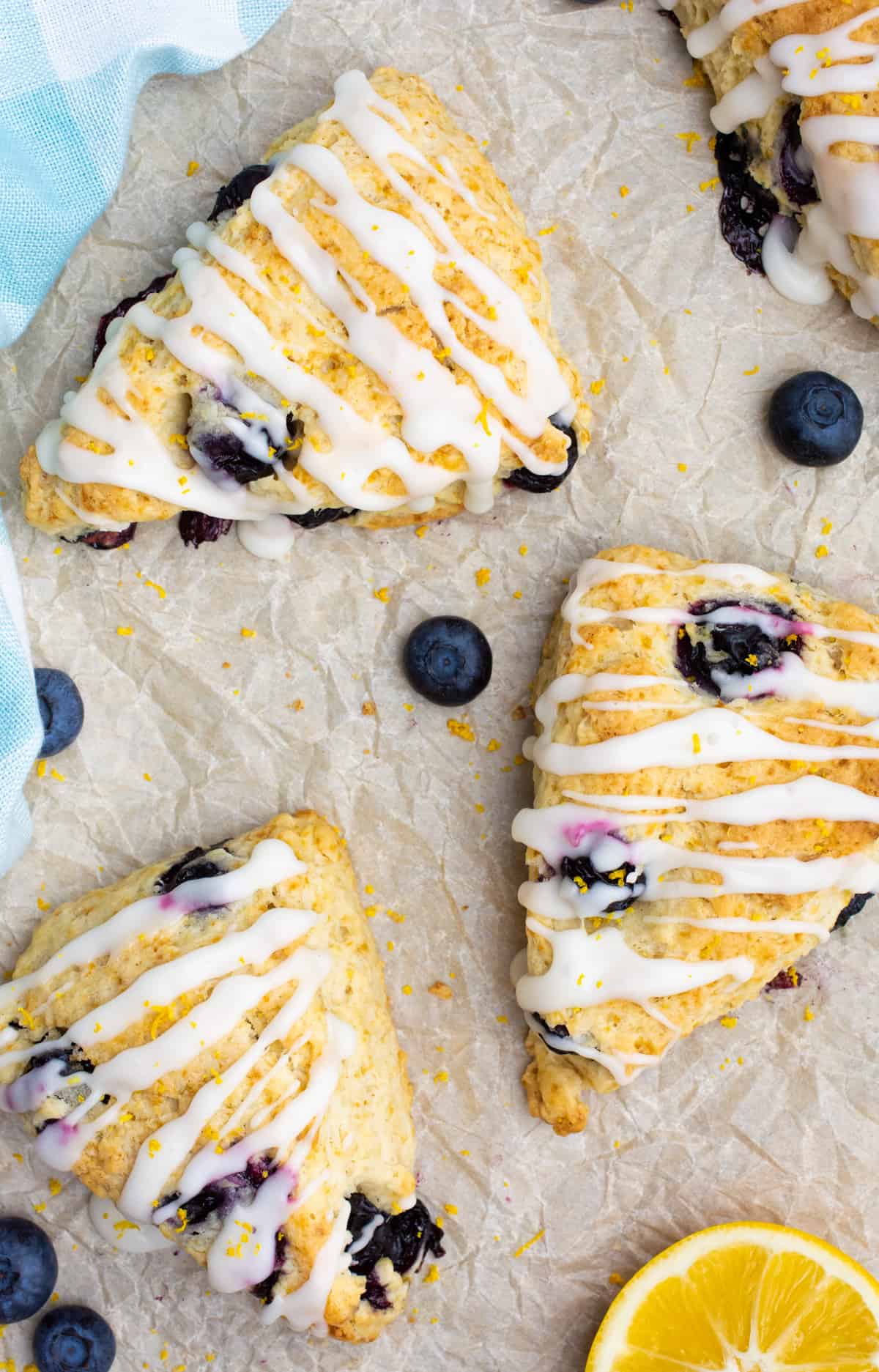 Blueberry scones topped with icing on brown parchment paper.
