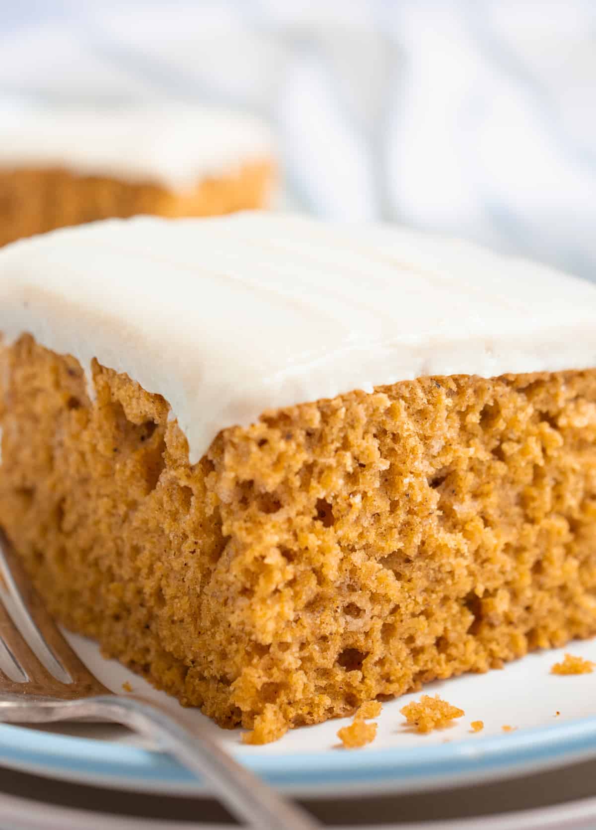 A slice of frosted vegan pumpkin cake on a plate with a fork.