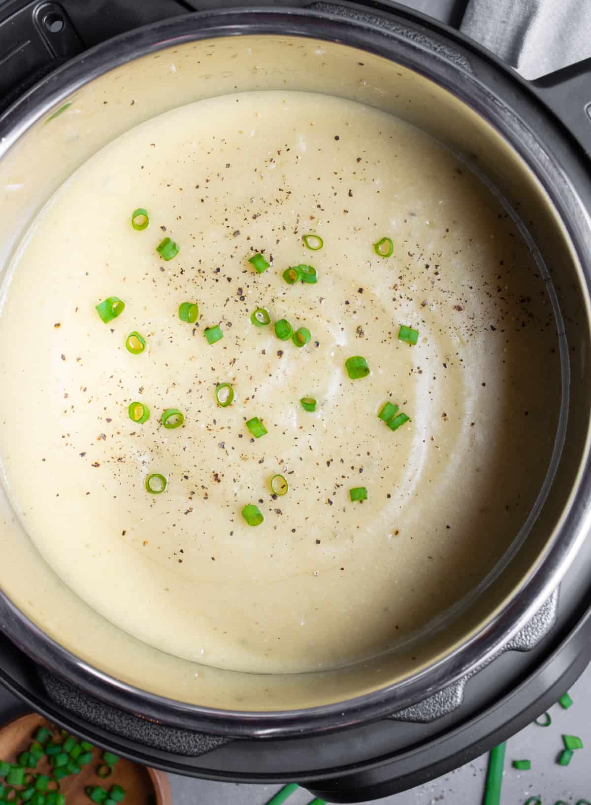 Creamy vegan potato soup in an Instant Pot topped with green onions and fresh pepper.