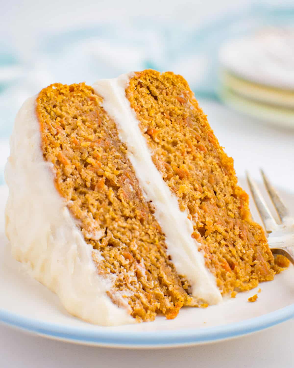 A two layer vegan carrot cake with vanilla frosting on a white plate.