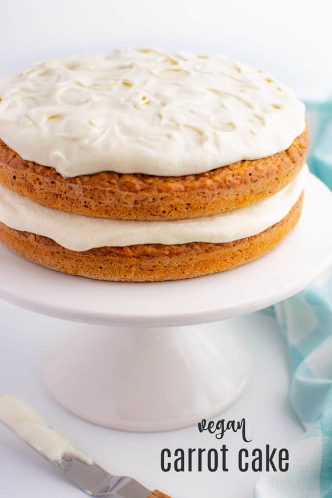 Two layer vegan carrot cake with cream cheese frosting on a white cake stand.