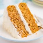 A wedge of 2 layer carrot cake with frosting on its side on a white plate.