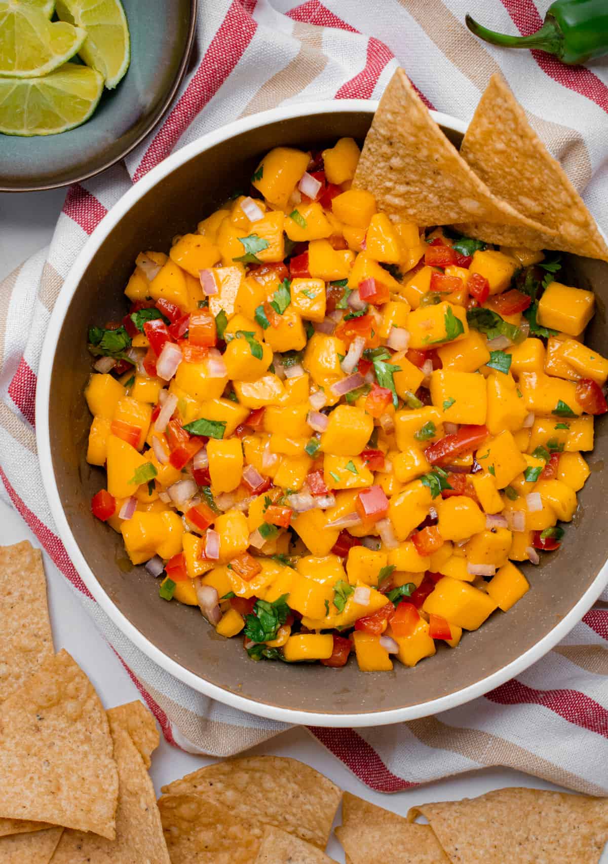 A brown bowl filled with mango salsa and surrounded by tortilla chips.