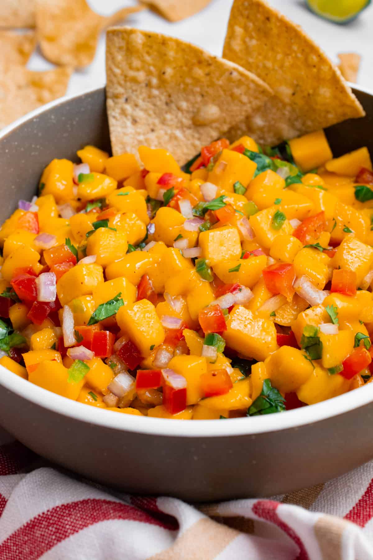 A bowl of mango salsa with 2 chips dipped in.