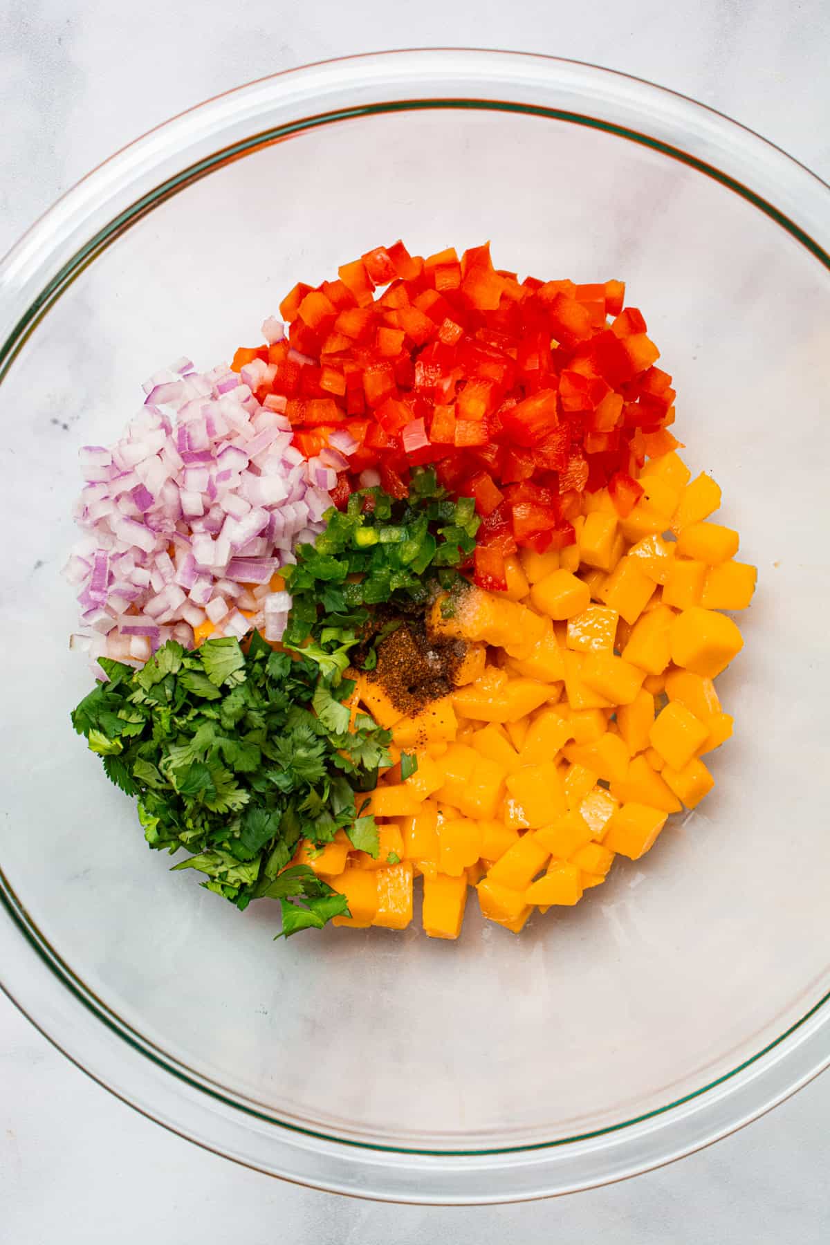 A glass bowl filled with diced mango, red onion, red bell pepper, cilantro, and jalapeño.