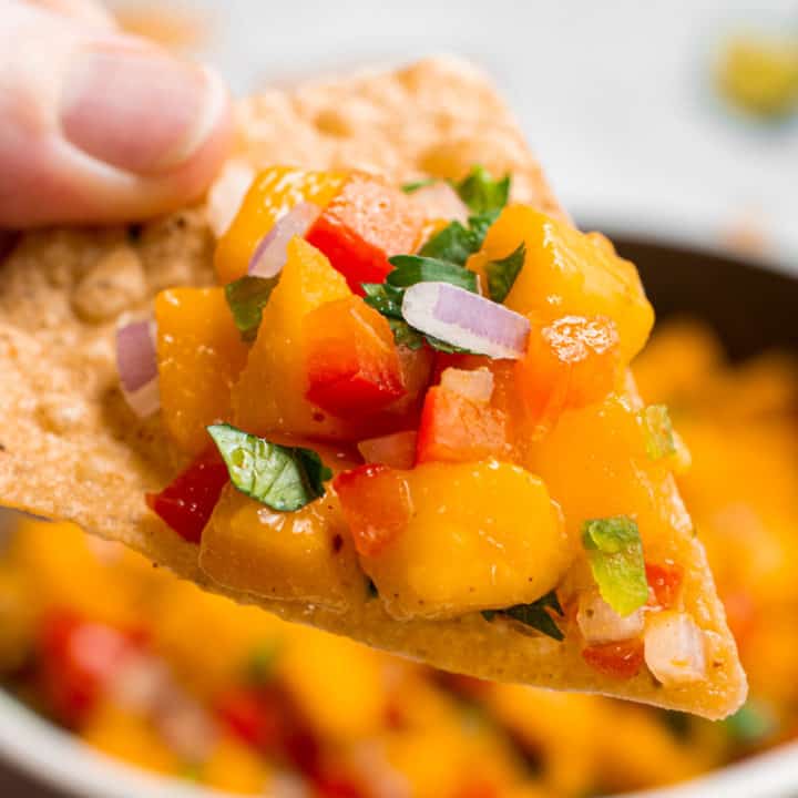 A hand holding a chip topped with mango salsa.