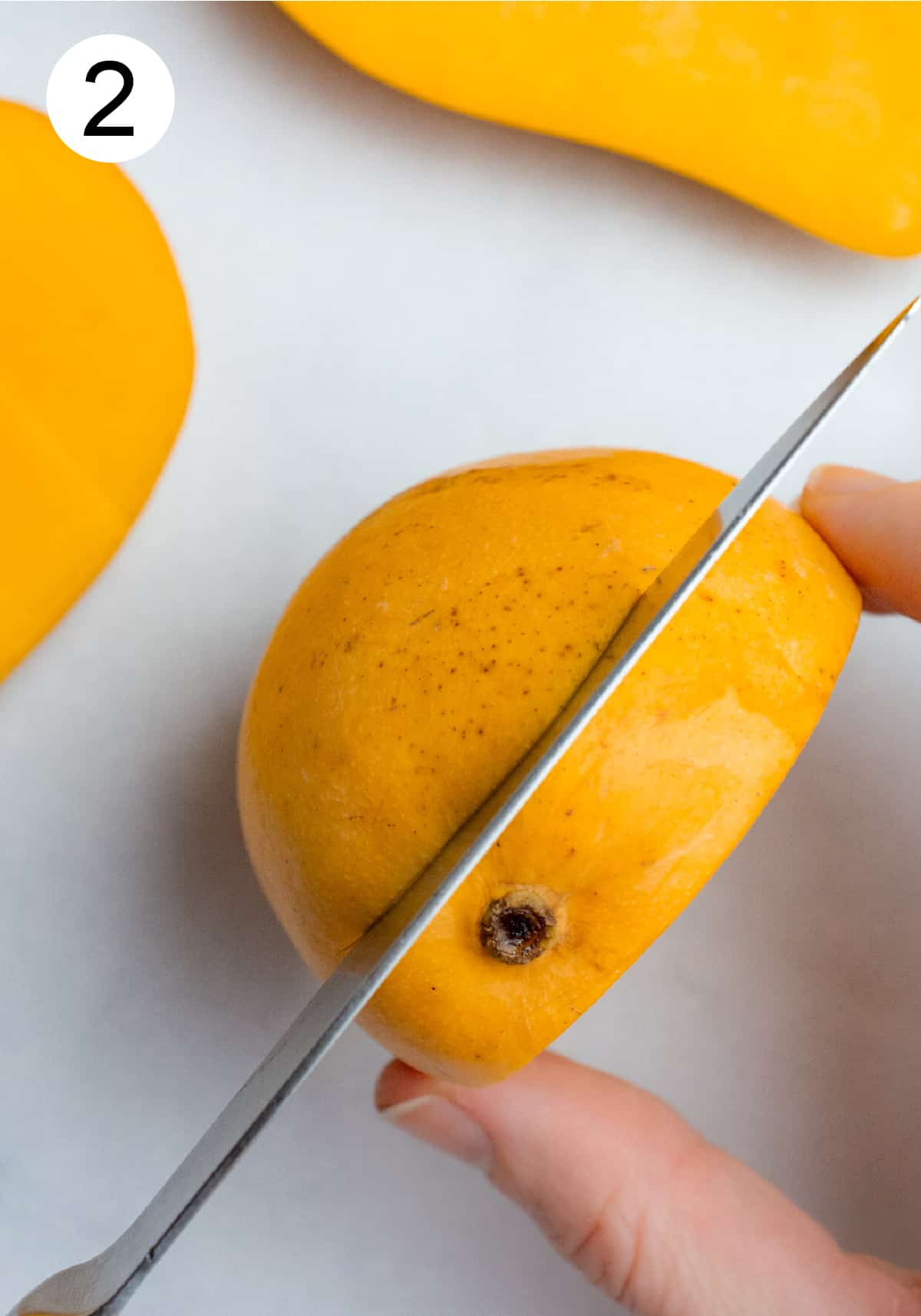 A knife cutting the flesh off one side of a mango.