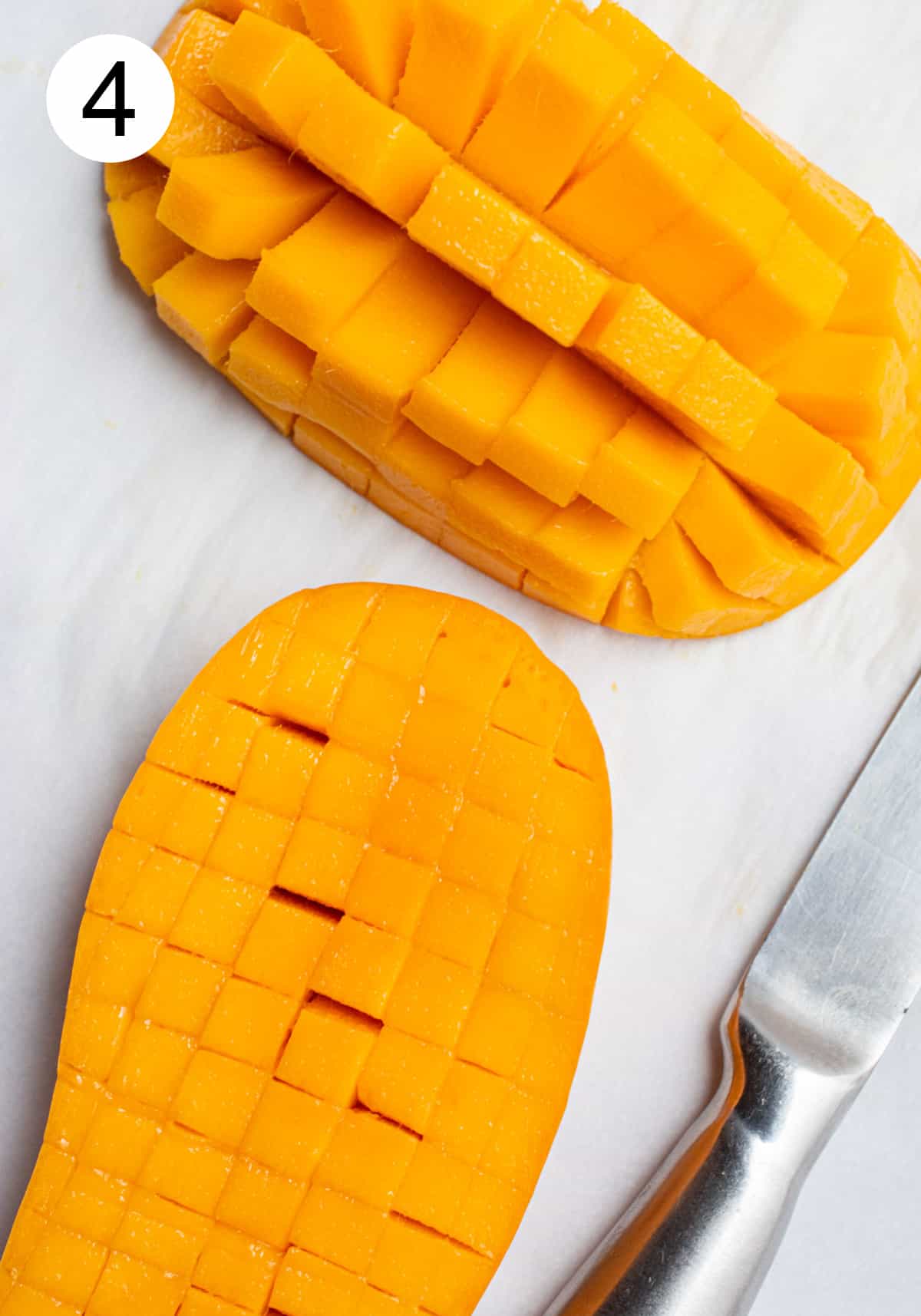 Two mango halves cut into cubes with one of the halves popped up.
