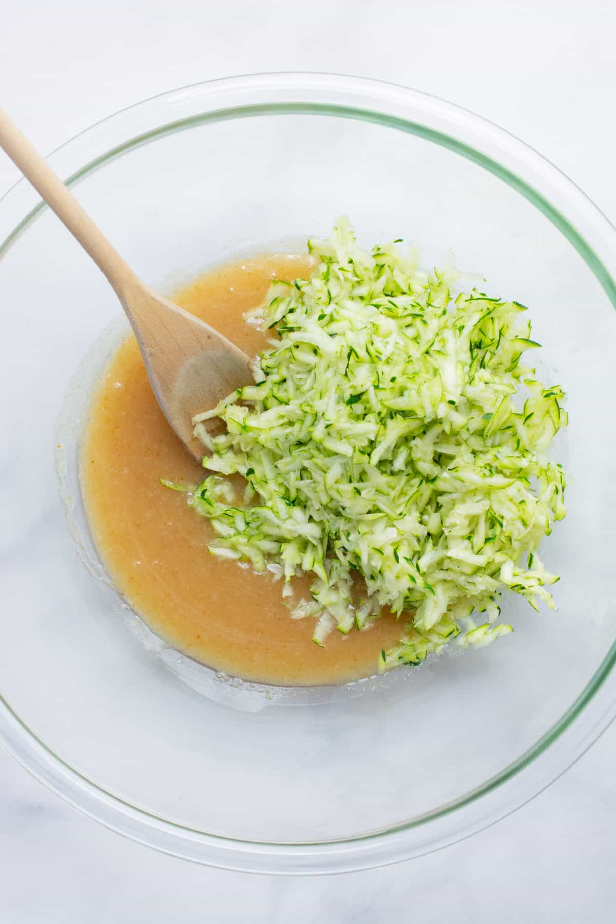 Wet ingredients and grated zucchini in a glass bowl.