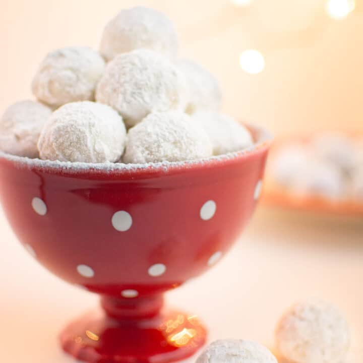 Vegan snowball cookies in a red serving dish with white dots.