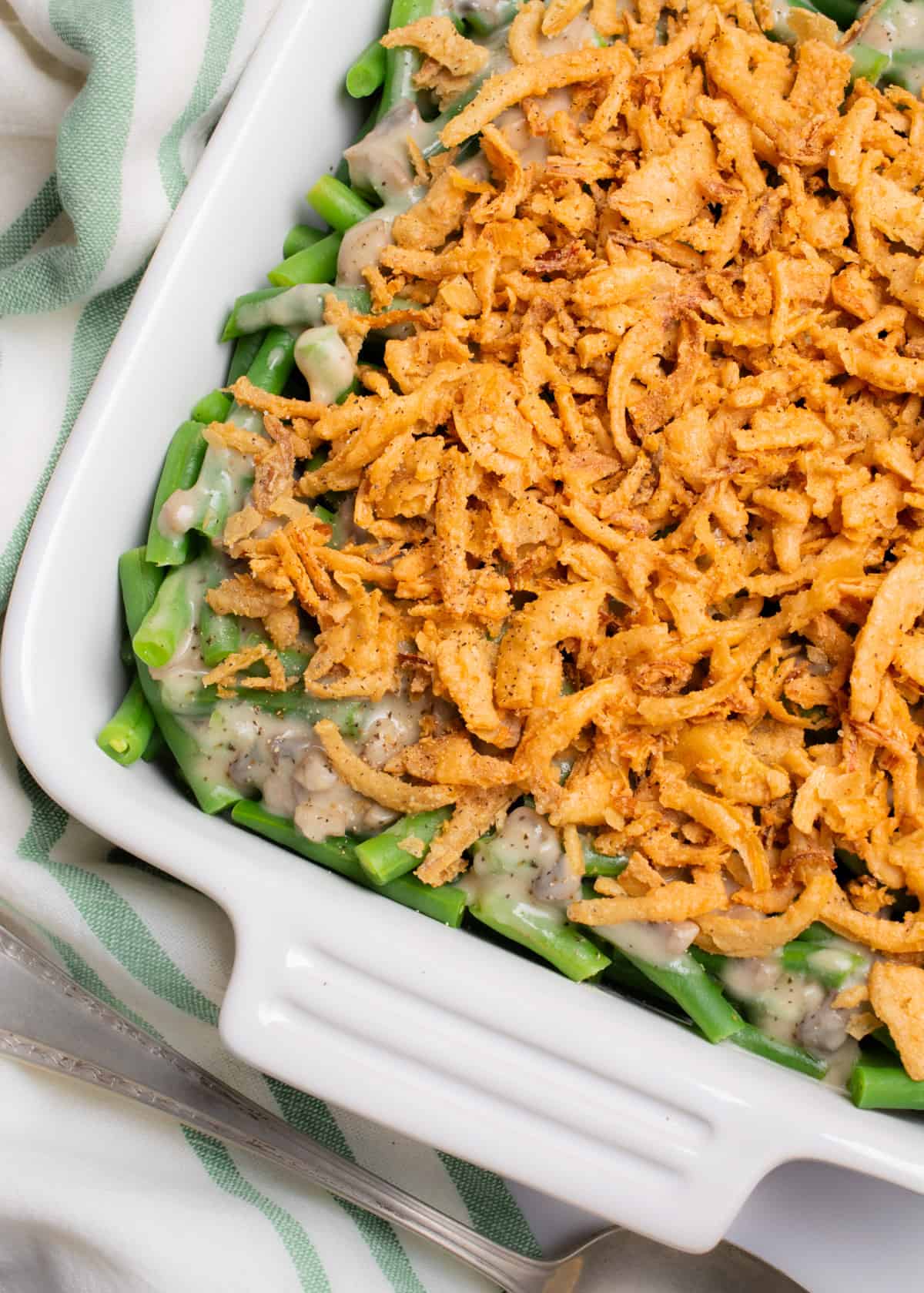 Vegan green bean casserole topped with fried onions in a white square baking dish.