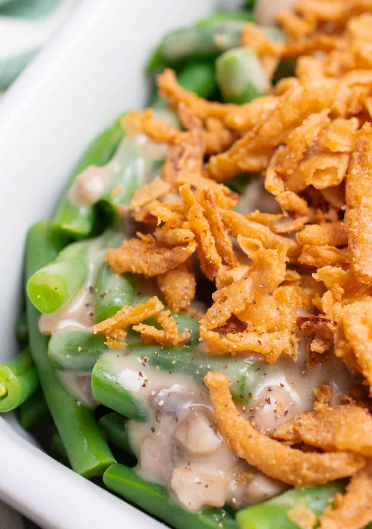 A close up of vegan green bean casserole. Green beans topped with vegan mushroom gravy and fried onions.