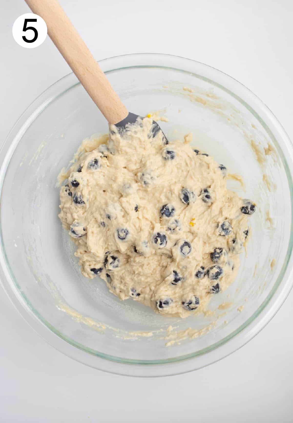 Vegan blueberry muffin batter mixed in a glass bowl with a spatula.