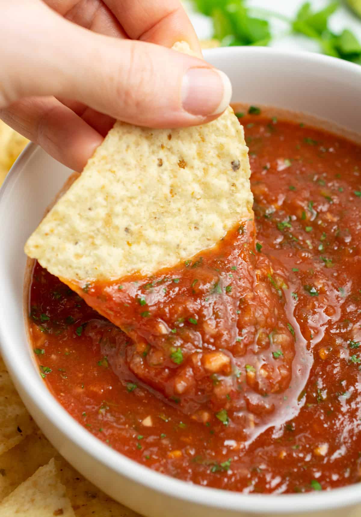 Homemade salsa in a bowl with a hand dipping a tortilla chip.
