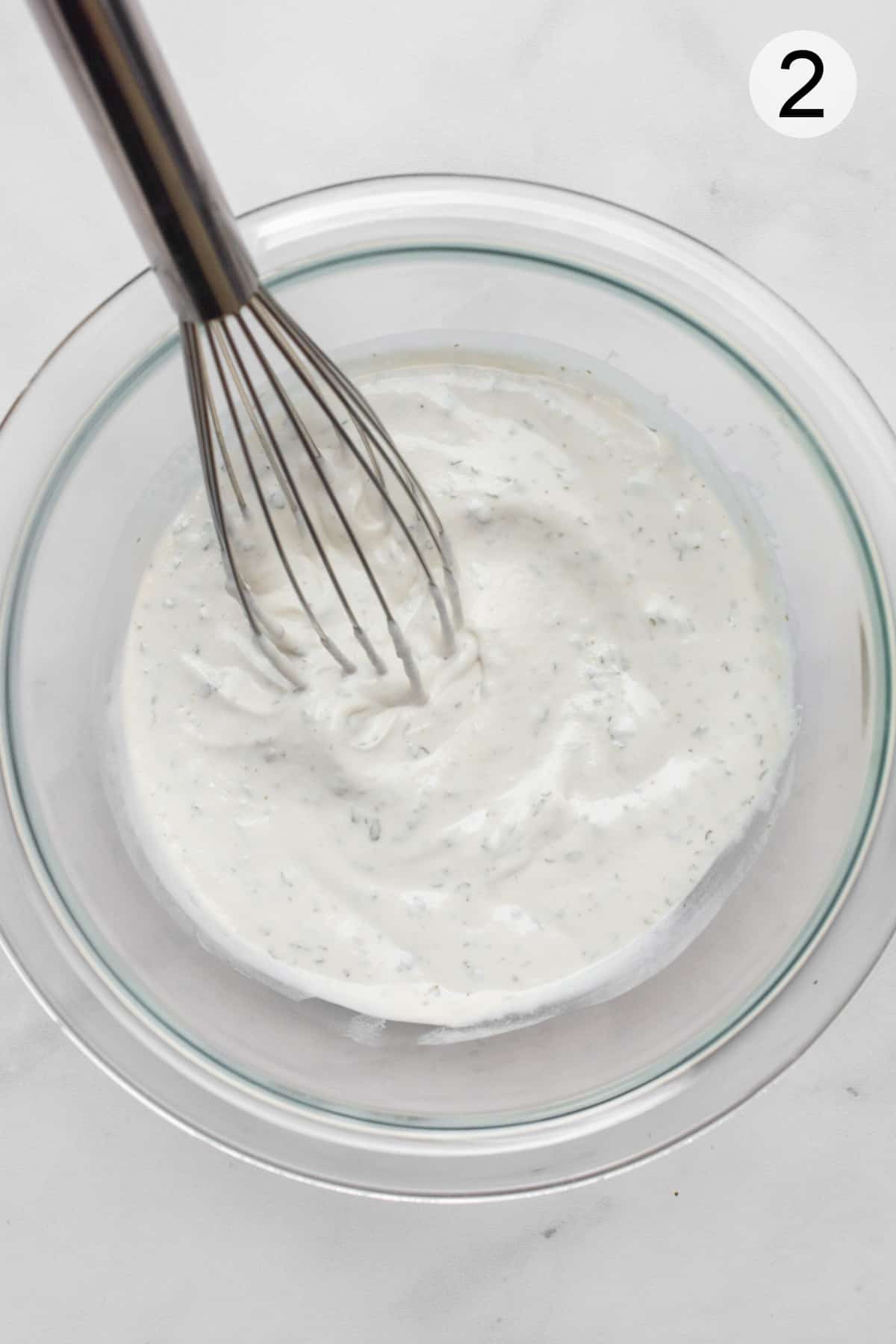 Ranch dip in a glass bowl with a metal whisk.