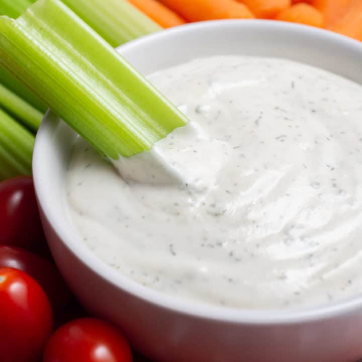 A bowl of vegan ranch dip with a celery stick dipped in.