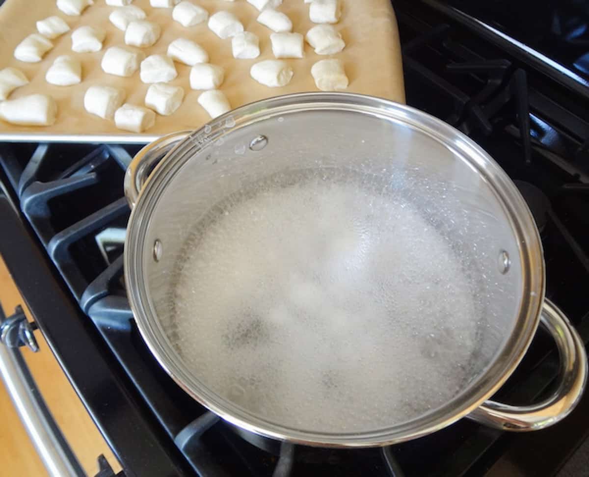 Baking soda and hot water in a pot with a pan of pretzel bites dough.