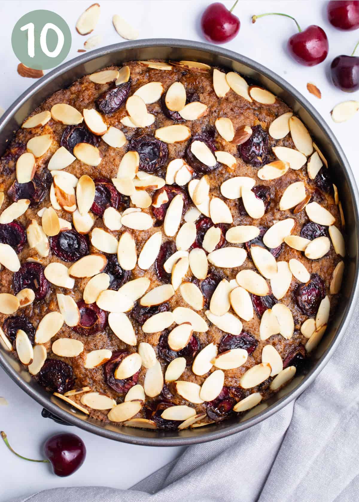 Vegan cherry coffee cake in a springform pan topped with halved cherries and sliced almonds after baking.
