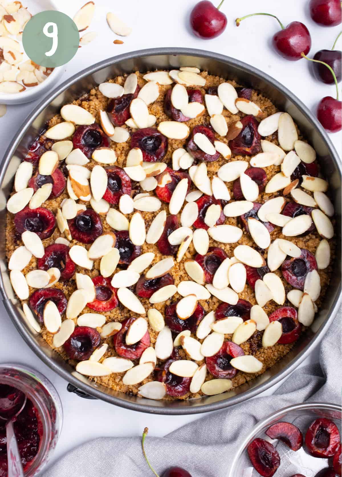 Coffee cake batter in a spring form pan topped with halved cherries and almond slices.